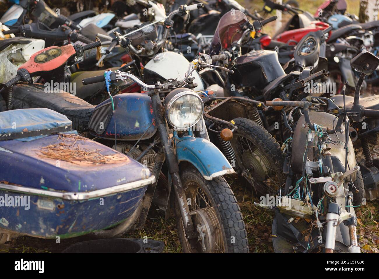 Die alten zerbrochenen rosteten Fahrräder, Motorräder, Spielzeugautos, Motoren, Reifen und Räder mit Speichen im Freien auf dem Boden Stockfoto