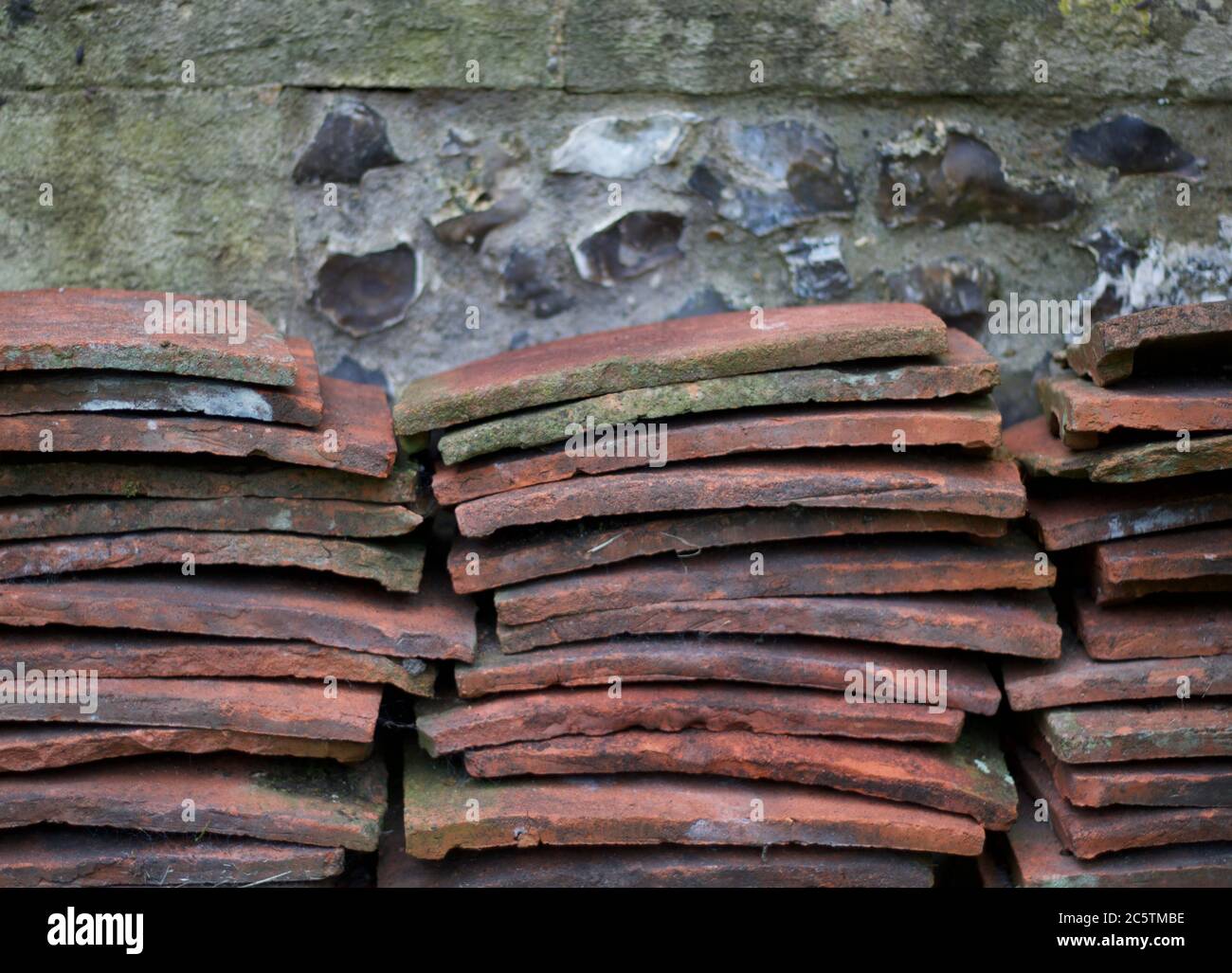 Stapel von alten Terrakotta-Dachziegeln gegen verwitterte Feuerstein Wand gestapelt Stockfoto