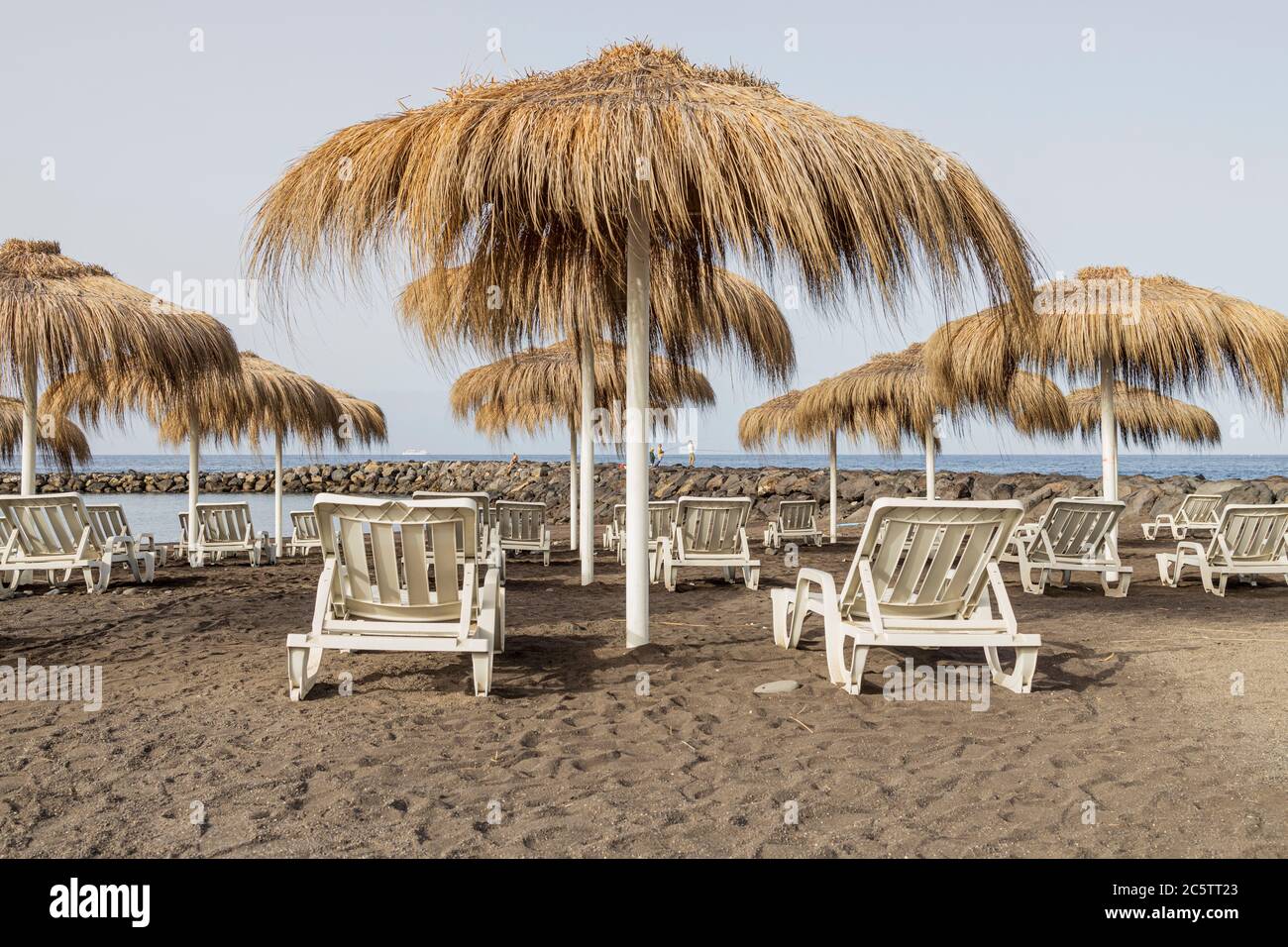 Costa Adeje, Teneriffa, Kanarische Inseln, Spanien. Juli 2020. Sonnenliegen und Strohschirme am Strand, da die ersten Touristen seit der Lockdo wieder ankommen Stockfoto