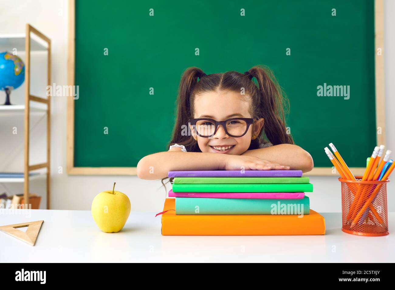 Lustige kleine Schülerin in Brille sitzt in einer Lektion in der Klasse in der Schule. Stockfoto