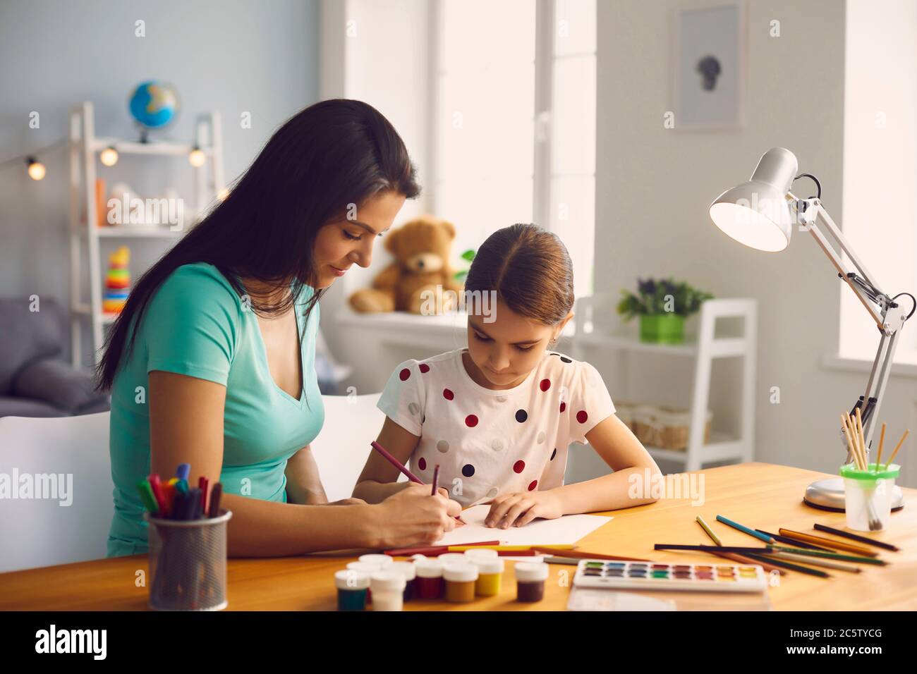 Frohe Familie. Das Kind zieht. Kleines Mädchen und Mutter zeichnen auf dem Tisch im Zimmer. Mutter lehrt Tochter zu zeichnen, während sitzen am Tisch zu Hause. Stockfoto