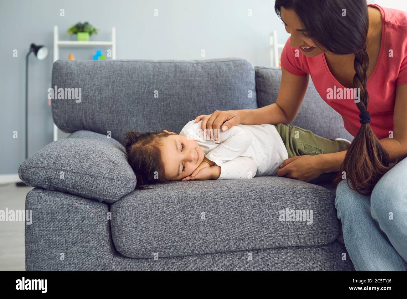 Glückliche junge Mutter, die ihre Tochter auf dem Sofa im Wohnzimmer schlafen sieht. Elternteil bewundert ihr schlappendes Kind zu Hause Stockfoto