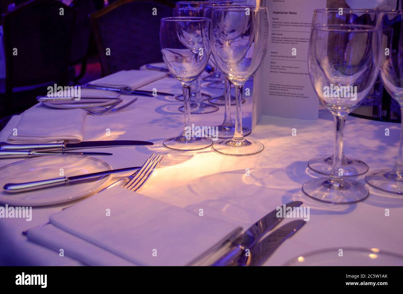 Ein gedeckter Tisch in einem Restaurant mit weißer Tischdecke, silbernem Besteck, Menü und Gläsern Stockfoto
