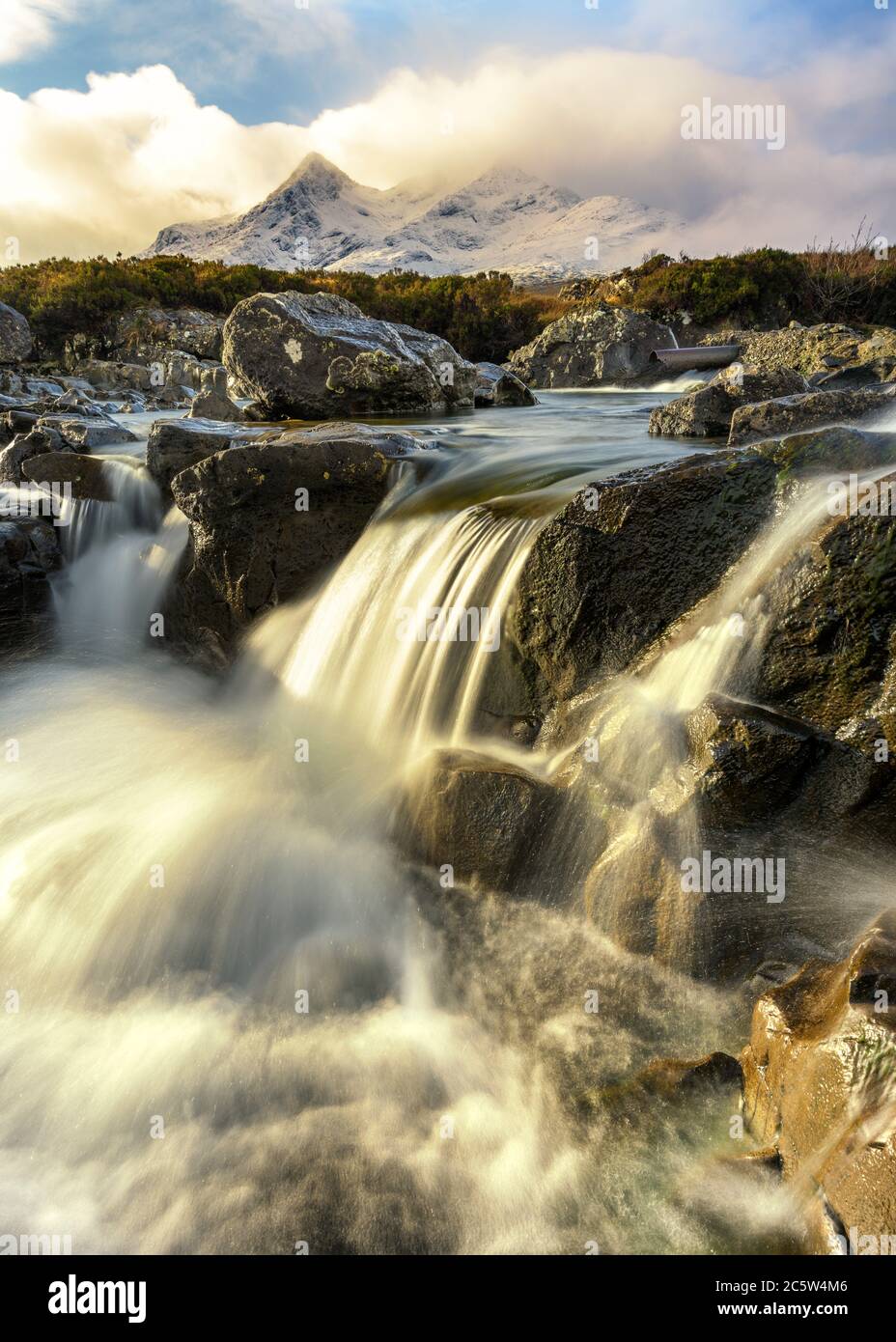 Fließender Wasserfall In Sligachan Mit Morgendlicher Sonneneinstrahlung Und Schottischen Schneebedeckten Bergen Im Hintergrund. Isle of Skye, Großbritannien. Stockfoto