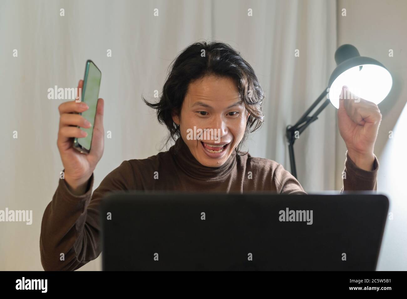 Asiatische Business Mann sieht sehr überrascht an seinem Laptop, sitzen Blick auf einige unglaubliche Nachrichten am Laptop-Bildschirm und überrascht gesturing erfolgreich Stockfoto