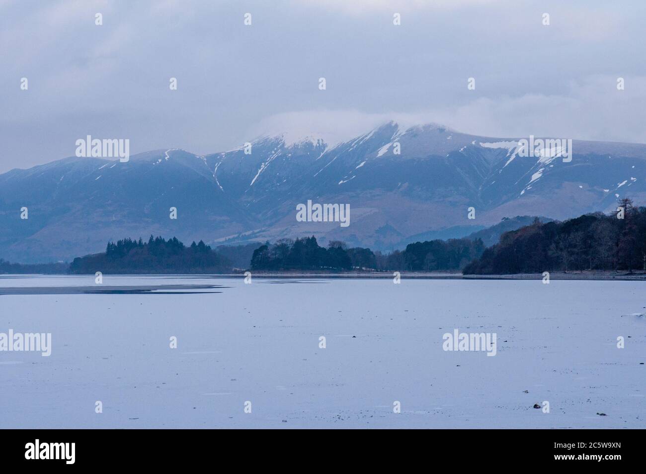 Schnee liegt an den Hängen des Skiddaw Berges über dem gefrorenen See Derwent Water im englischen Lake District. Stockfoto