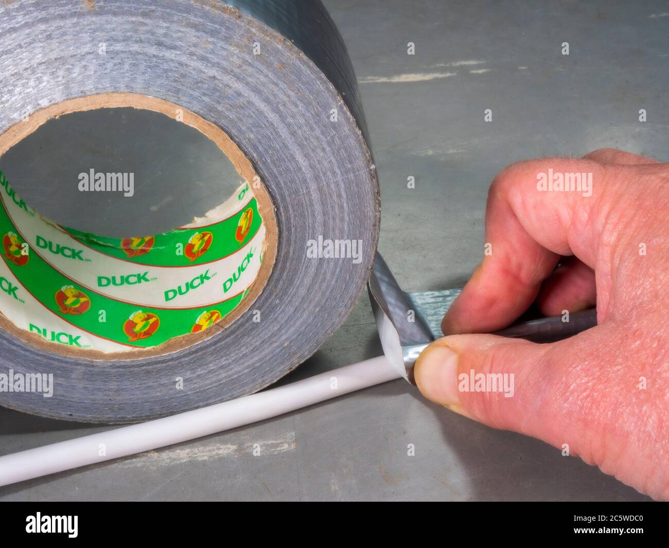 Nahaufnahme eines Mannes Finger und Daumen drücken einige Tuch-backed Klebstoff Duck / Kanal-Band von einer silbernen Rolle, über ein Netzkabel auf einem Vinyl-Boden. Stockfoto