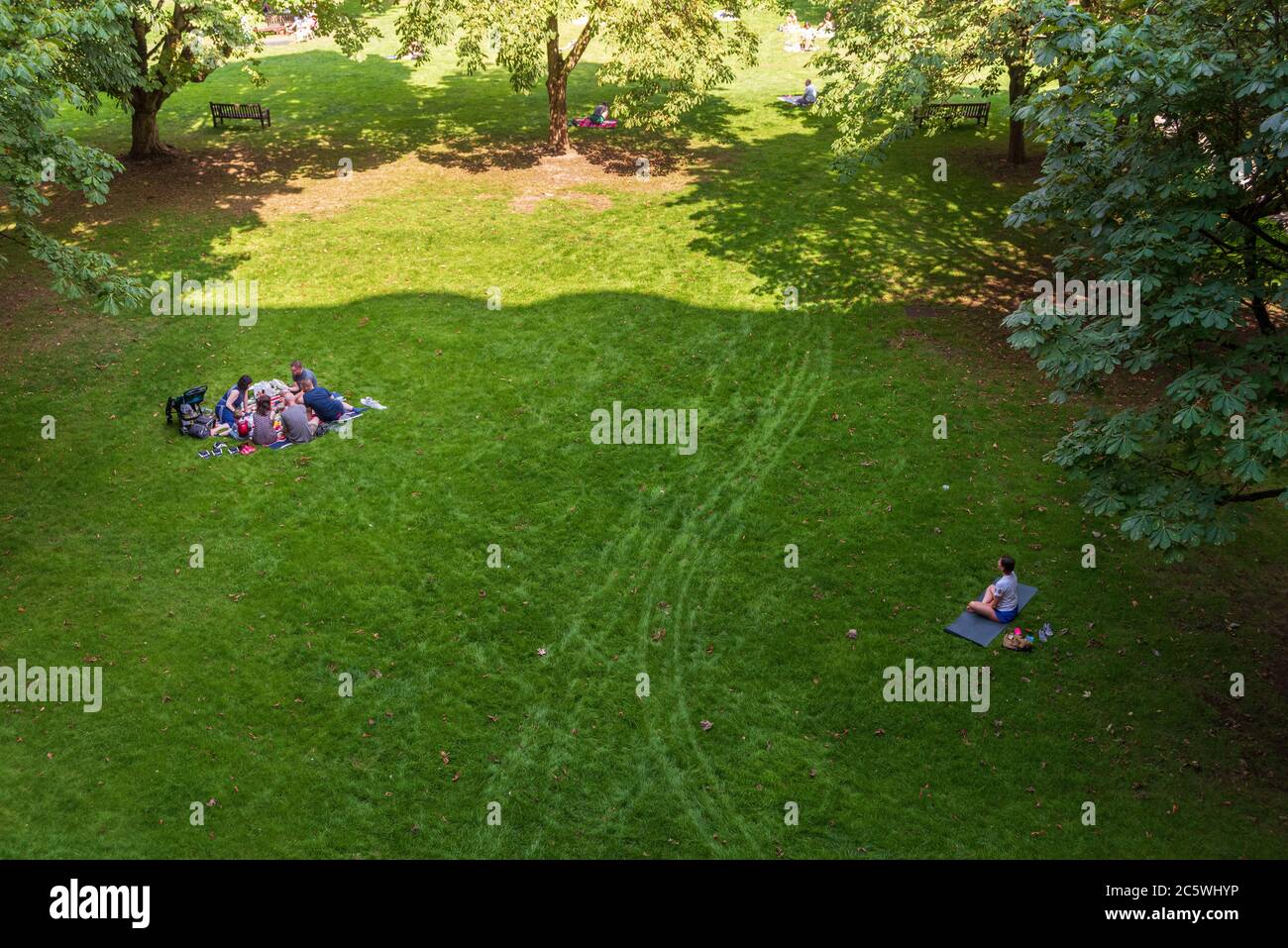 Zwei Gruppen von Menschen sitzen auf dem Rasen im Park. Die erste Gruppe macht ein Picknick, die zweite meditiert. Stockfoto