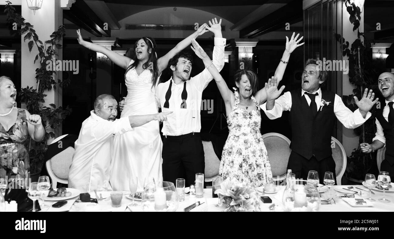 Hochzeit Chaos mit spontanem Singen & Tanzen am obersten Tisch einer Hochzeitsfeier oder Hochzeitsfrühstück. Hochzeitsfeier. Schwarz-Weiß-Reportage. Stockfoto