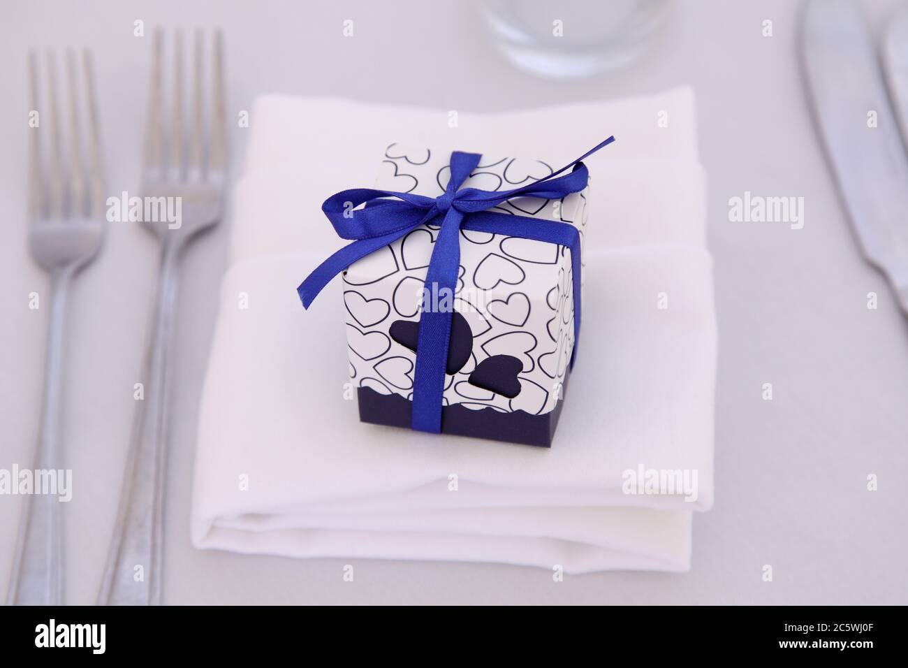 Kleines Geschenk in einem blauen Band mit Schleife auf Esstisch mit Besteck & Serviette verpackt. Hochzeit Bevorzugung oder Hochzeit Bevorzugungen auf weißem Hintergrund. Stockfoto