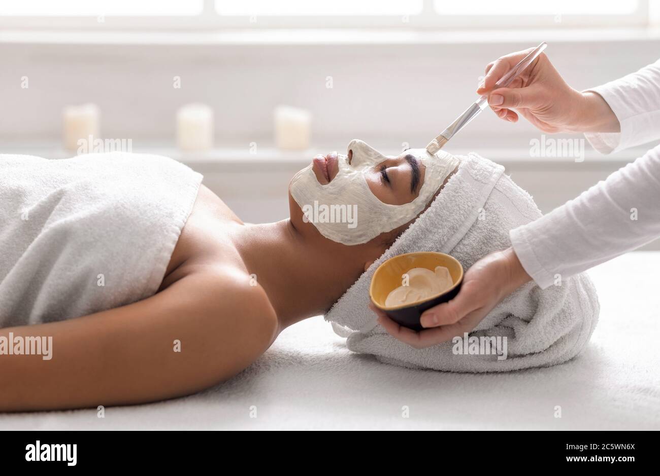 Kosmetikerin setzt weiße Tonmaske auf schlafende Frau Gesicht Stockfoto