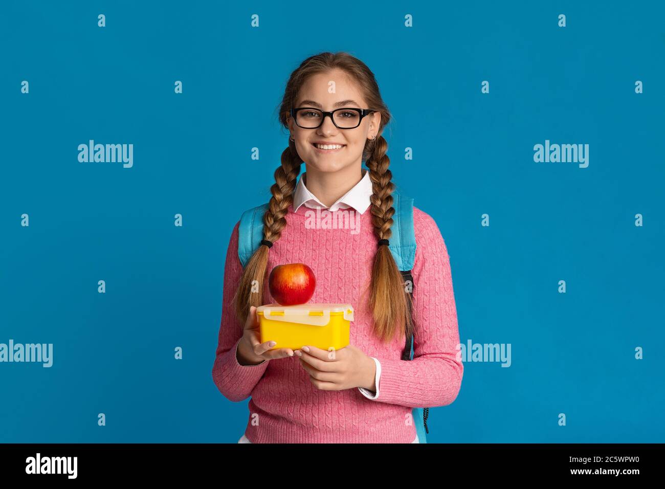 Mittagessen in der Schule. Lächelndes Teenager-Mädchen in Gläsern hält Essen in Behälter und Apfel Stockfoto