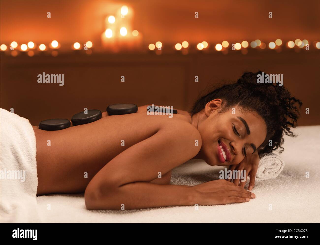 Entspannte afrikanische Mädchen genießen heiße Steine Massage im Spa Stockfoto