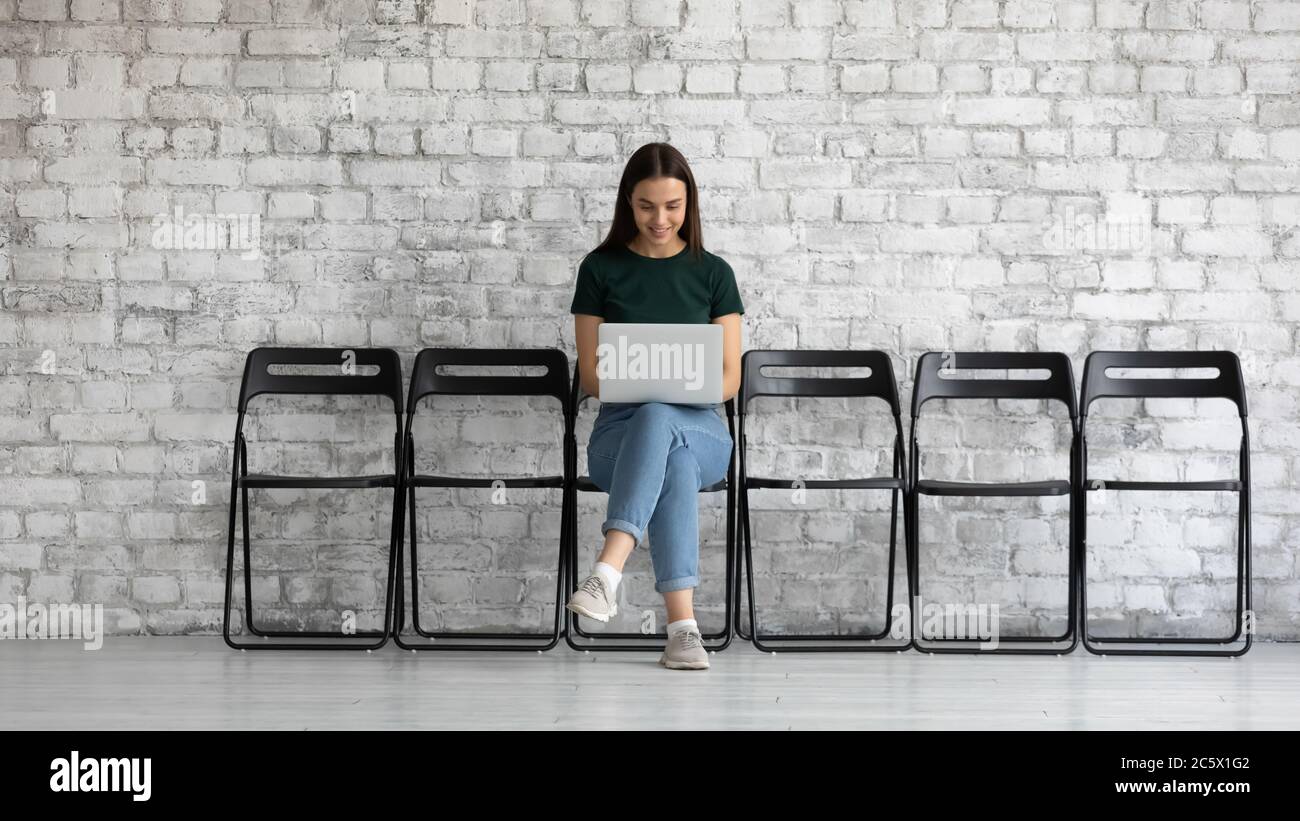 Studentin mit Laptop sitzen auf einem Stuhl im Büroflur Stockfoto