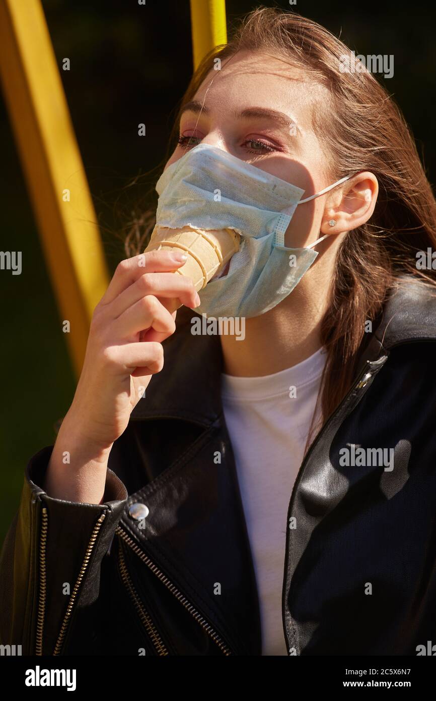 Fun junge Frau tragen medizinische Maske mit Loch und isst Eis Stockfoto