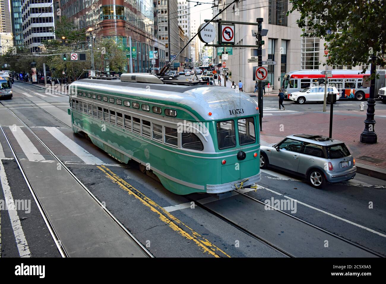 Ein hellgrüner Vintage-Trolley fährt entlang der Marktstraße in der Innenstadt von San Francisco. Ein silberner Mini ist neben dem Trolley und moderne Bus ist in der Nähe. Stockfoto