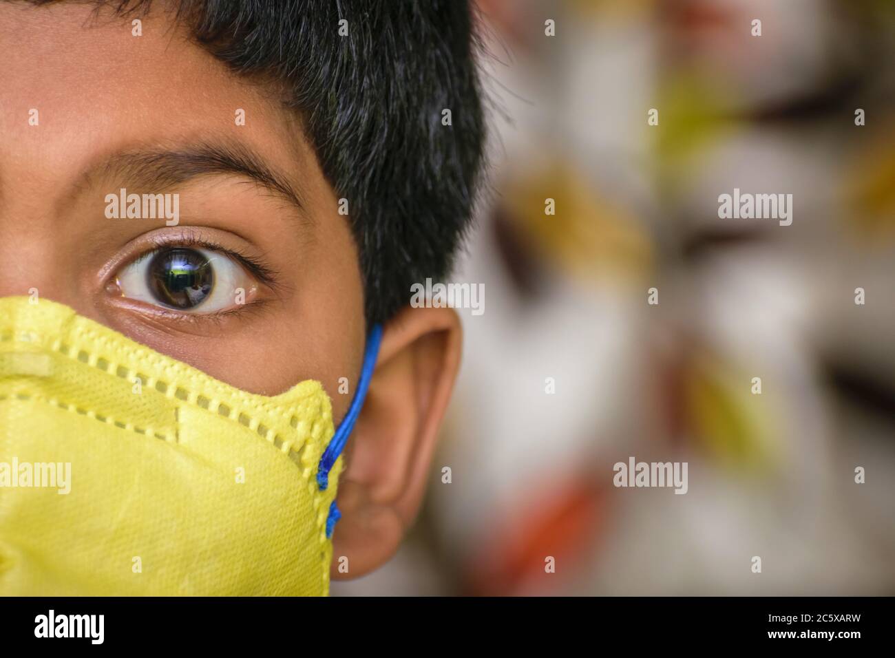 Isolierter junger indischer Junge mit prominenten Augen, die eine Gesichtsmaske N95 tragen, um gegen Covid 19 zu schützen. Platz für Text rechts Stockfoto