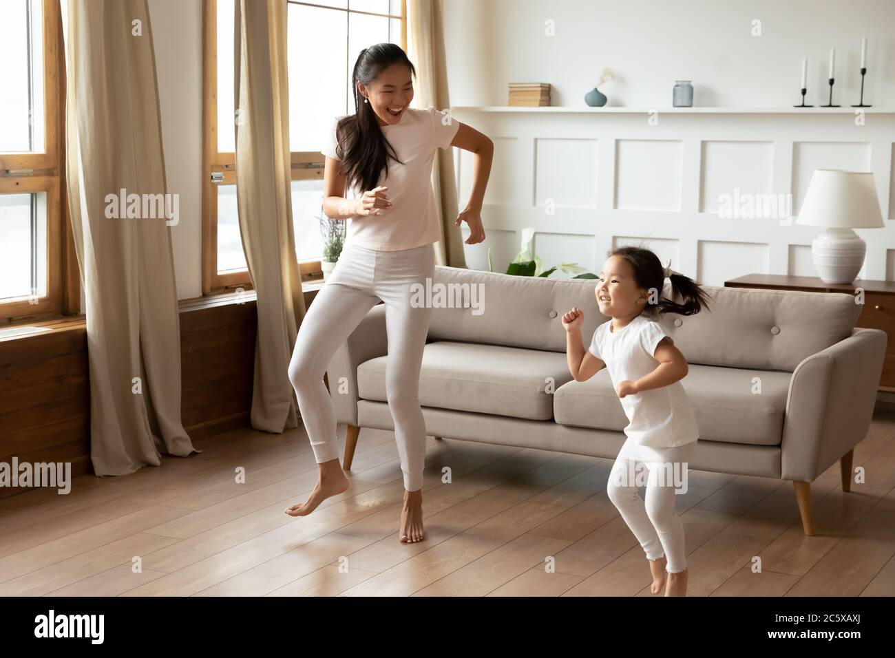 Energische junge vietnamesische ethnische Mutter tanzen mit Kind Tochter. Stockfoto