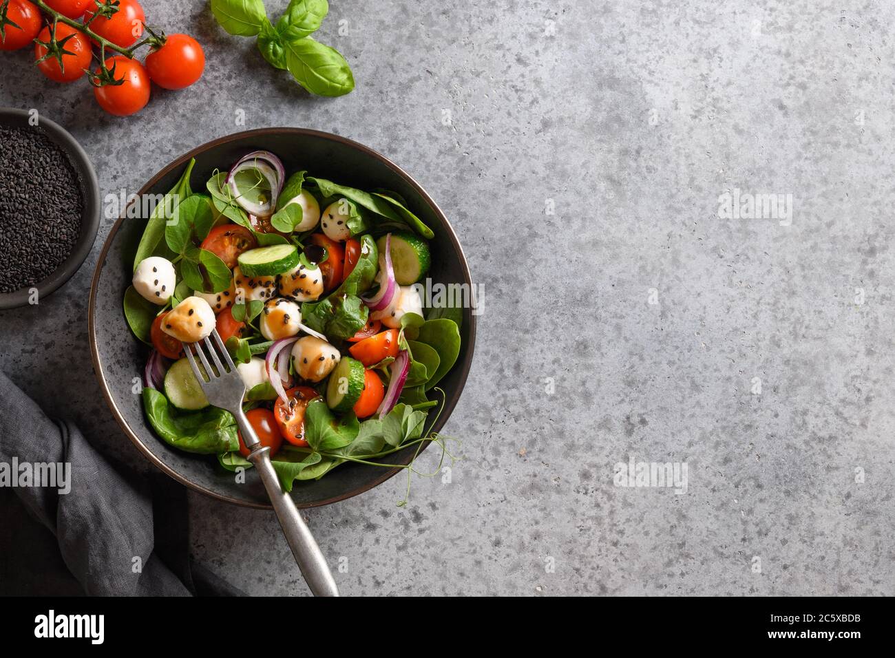 Salat mit Spinat, Kirschtomaten, Zwiebel und Mozzarella auf grauem Steingrund. Draufsicht. Stockfoto