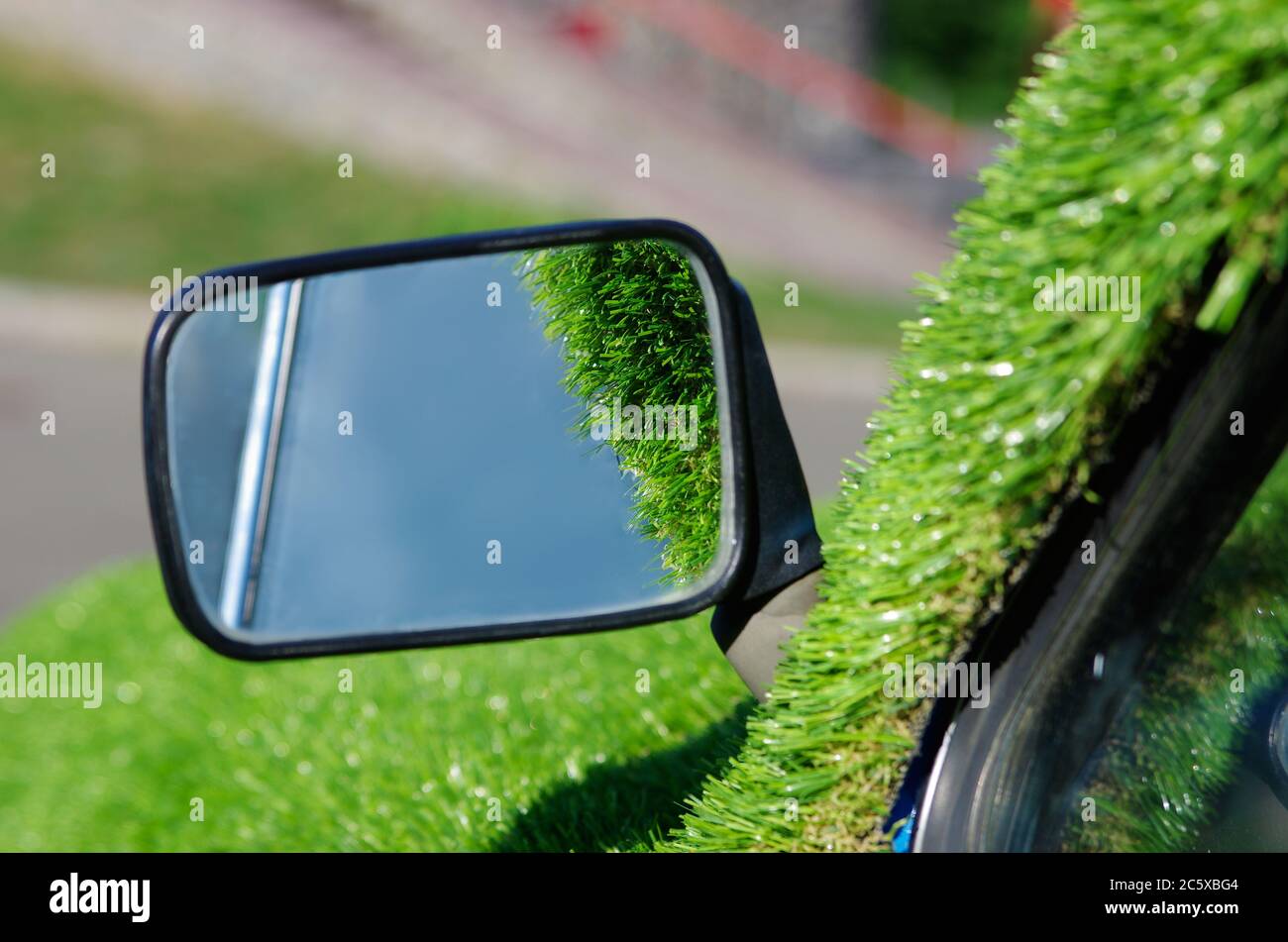 Autospiegel mit grünem Kunstrasen herum. Spiegelung des Himmels. Emissionsfreie Fahrzeugkonzeption Stockfoto