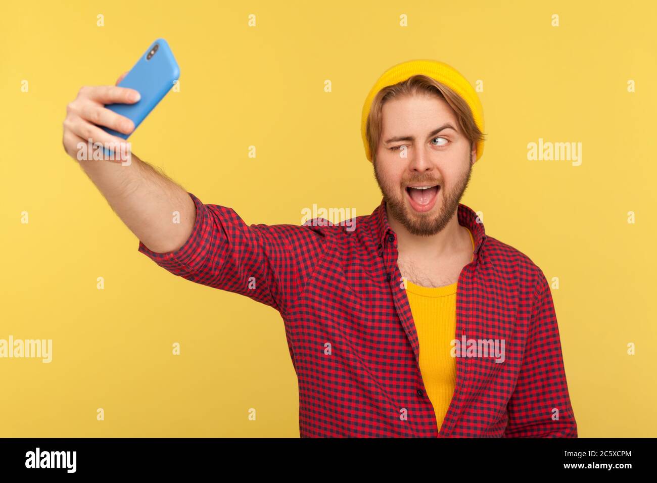 Lustige sorglose Hipster Kerl in karierten Shirt machen verrückte Gesicht, zwinkert zum Handy, komisch dumm Grimasse und Selfie auf Handy Stockfoto