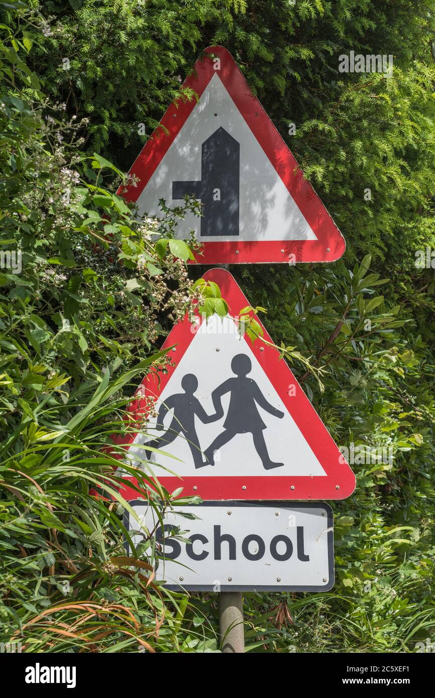 Ländliche Land Schule dreieckiges Warnschild in Straßenhecke. UK Junge und Mädchen zu Fuß Piktogramm für Sicherheitsbewusstsein. Metapher zurück in die Schule. Stockfoto