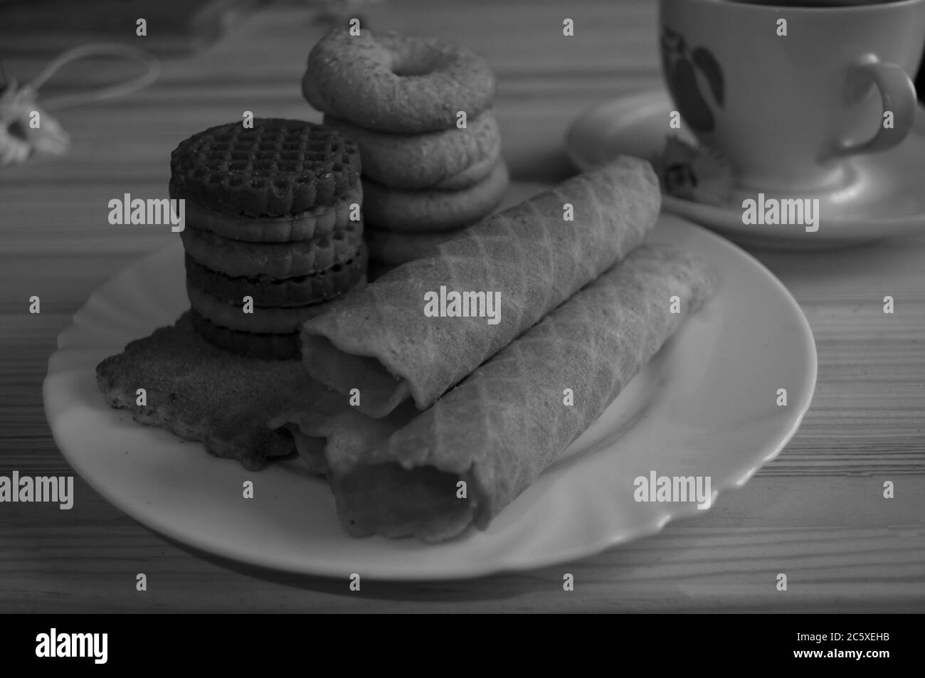 Waffelbrötchen und Kekse auf einem weißen Teller und eine Tasse Kaffee. Waffeln auf der Seite. Komposition auf einem hölzernen Hintergrund. Sichtbare Waffelstruktur, Holz Stockfoto