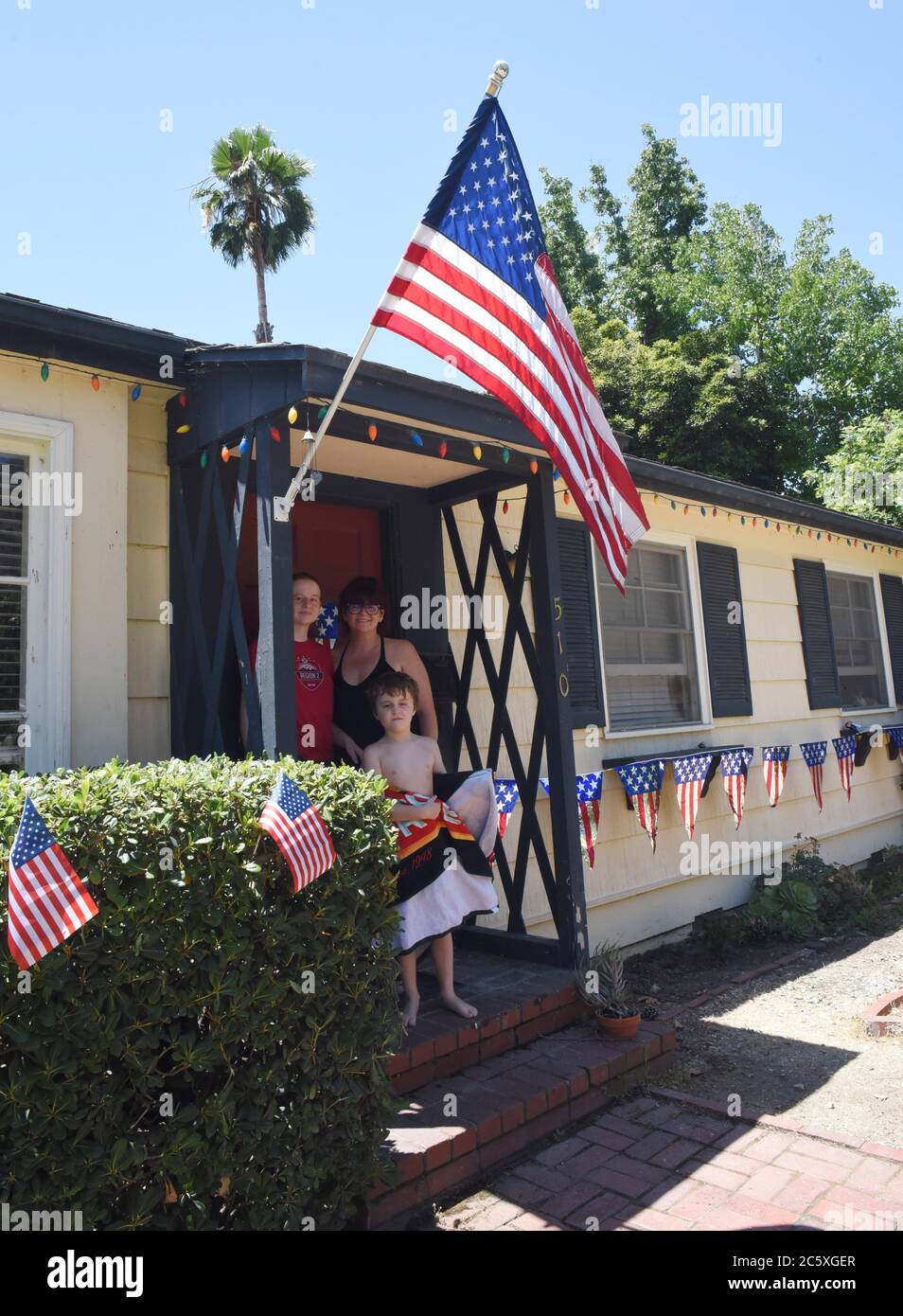 Sierra Madre, Kalifornien, USA. Juli 2020. Mel Smoron (ganz rechts), ihre Tochter Naomi Smoron (links) und ihr Sohn in der Mitte, Merek Smoron schauen aus ihrer Tür hoffentlich auf die Stadt Dekorationskomitee, als sie auf Golfwagen patriotisch geschmückt ankommen, um ihr Haus zu beurteilen. Sie nahm am Wettbewerb um das bestdekorierte Haus zu gewinnen. Die Hoffnung ist mit der Familie Smoron angesichts der Pandemie noch lebendig. Kredit: Catherine Bauknight/ZUMA Wire/Alamy Live Nachrichten Stockfoto Sierra Madre, Kalifornien, USA. Juli 2020. Mel Smoron (ganz rechts), ihre Tochter Naomi Smoron (links) und ihr Sohn in der Mitte, Merek Smoron schauen aus ihrer Tür hoffentlich auf die Stadt Dekorationskomitee, als sie auf Golfwagen patriotisch geschmückt ankommen, um ihr Haus zu beurteilen. Sie nahm am Wettbewerb um das bestdekorierte Haus zu gewinnen. Die Hoffnung ist mit der Familie Smoron angesichts der Pandemie noch lebendig. Kredit: Catherine Bauknight/ZUMA Wire/Alamy Live Nachrichten Stockfoto