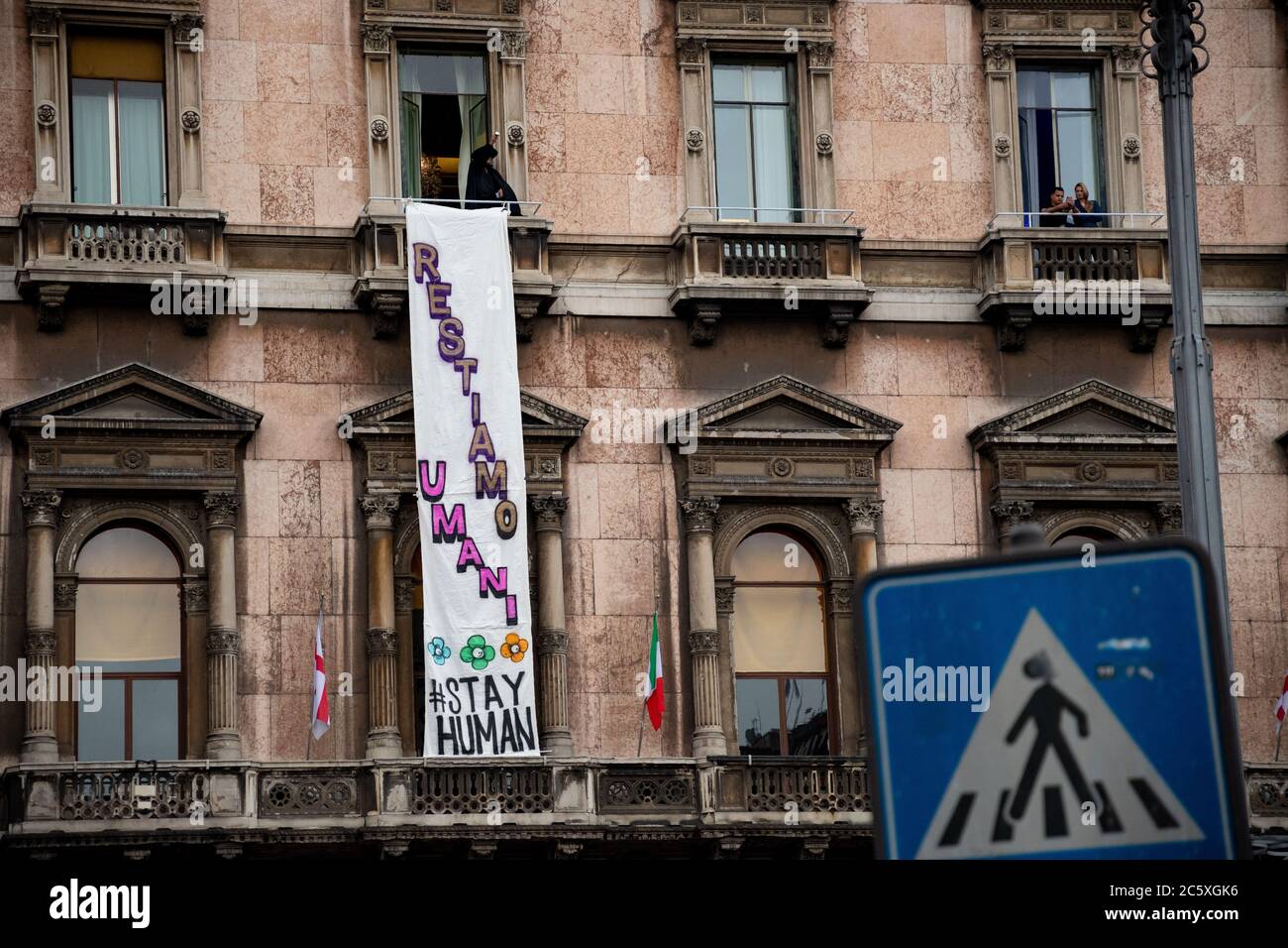 Auf einem Balkon über der Piazza del Duomo trägt ein Aktivist ein Zorro-Kostüm, das während eines politischen Treffens mit Matteo Salvini ein Protestbanner zeigt. Stockfoto