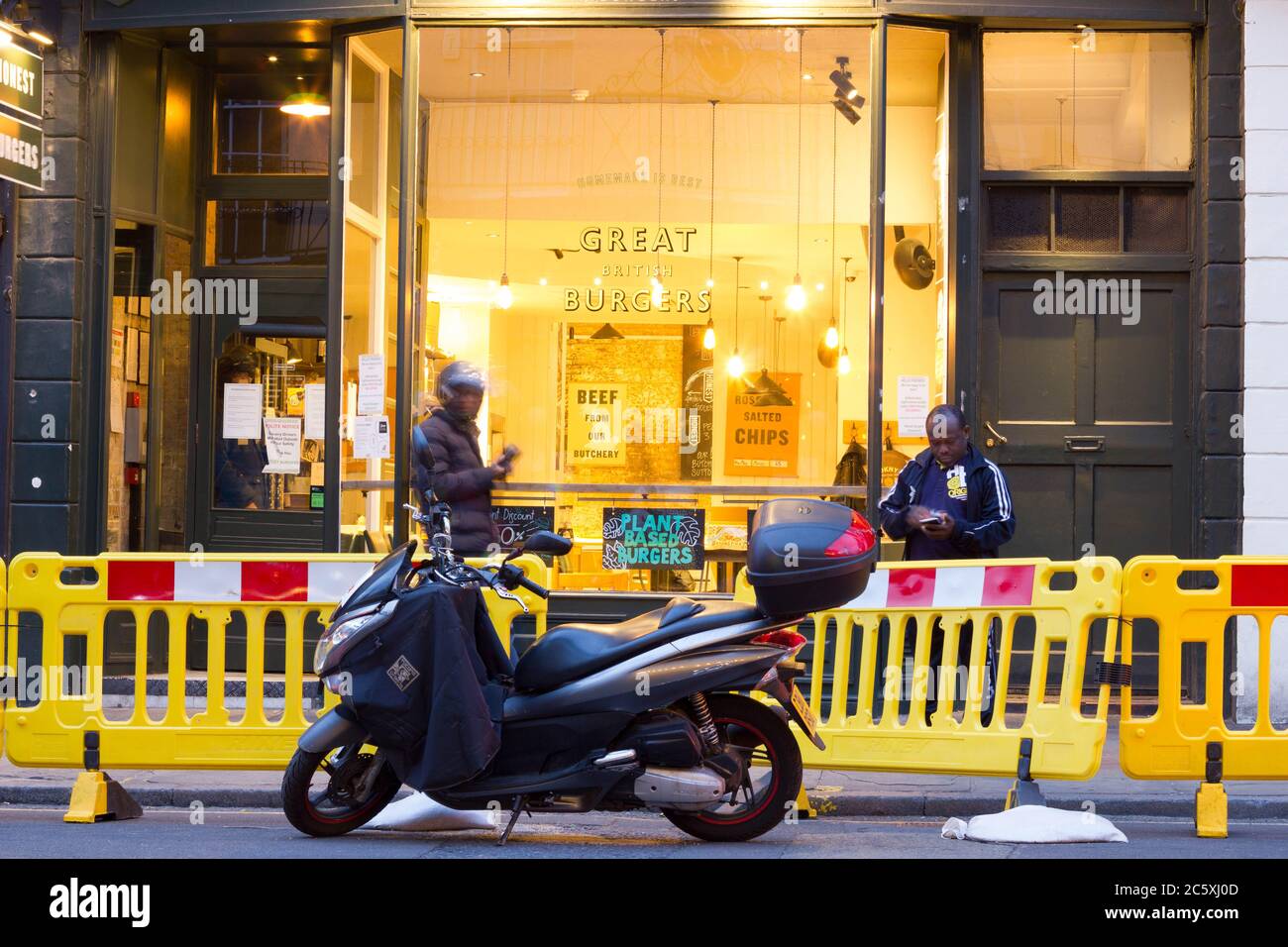 Zwei Take-away-Lieferer und Fahrräder warten vor dem Burger-Shop in Greenwich, London, England Stockfoto