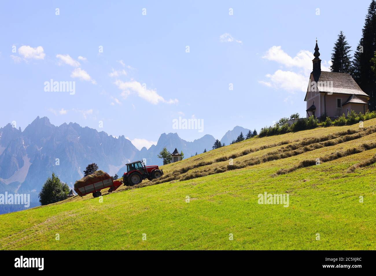 Romantische alpine ländliche Landschaft mit Traktor sammeln Heu und neblig Berge im Hintergrund mit Platz für Ihren Text Stockfoto
