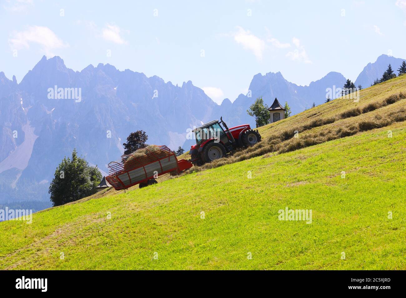 Romantische alpine ländliche Landschaft mit Traktor sammeln Heu und neblig Berge im Hintergrund mit Platz für Ihren Text Stockfoto