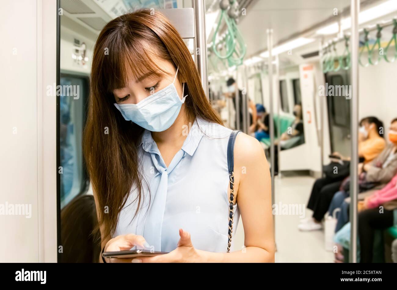 Junge asiatische Frau Passagier trägt chirurgische Maske und mit Handy in U-Bahn-Zug Stockfoto