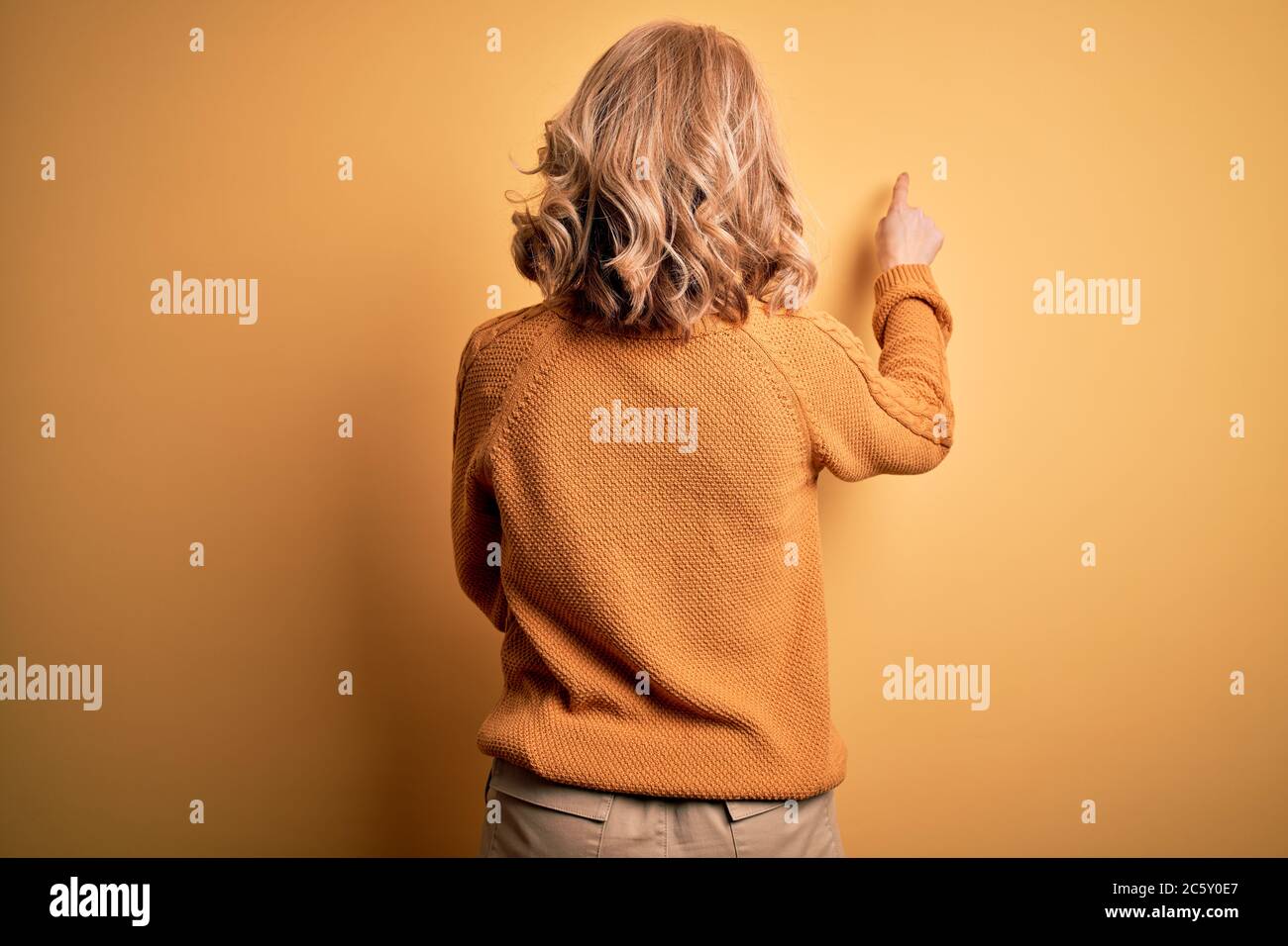 Mittelalter schöne blonde Frau trägt lässige Pullover und Brille über  gelben Hintergrund posiert rückwärts zeigt nach vorne mit der Fingerhand  Stockfotografie - Alamy
