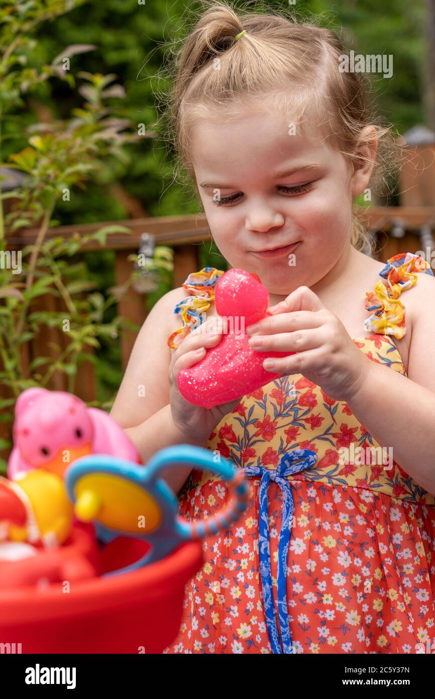 Drei Jahre altes Mädchen, das Spaß mit ihrem draußen Wasserspielzeug hat, besonders ihr rotes duckie Stockfoto