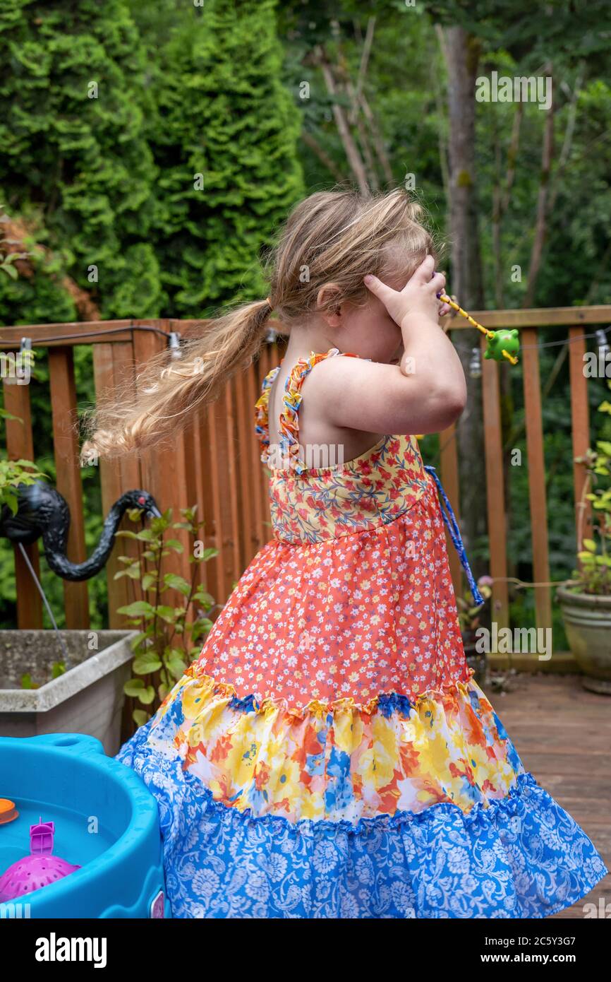 Drei Jahre alt Spaß haben spielen draußen Spaß Spinnen in Kreisen außerhalb mit einem ihrer Wasserspielzeug an ihrem Forhead gehalten Stockfoto