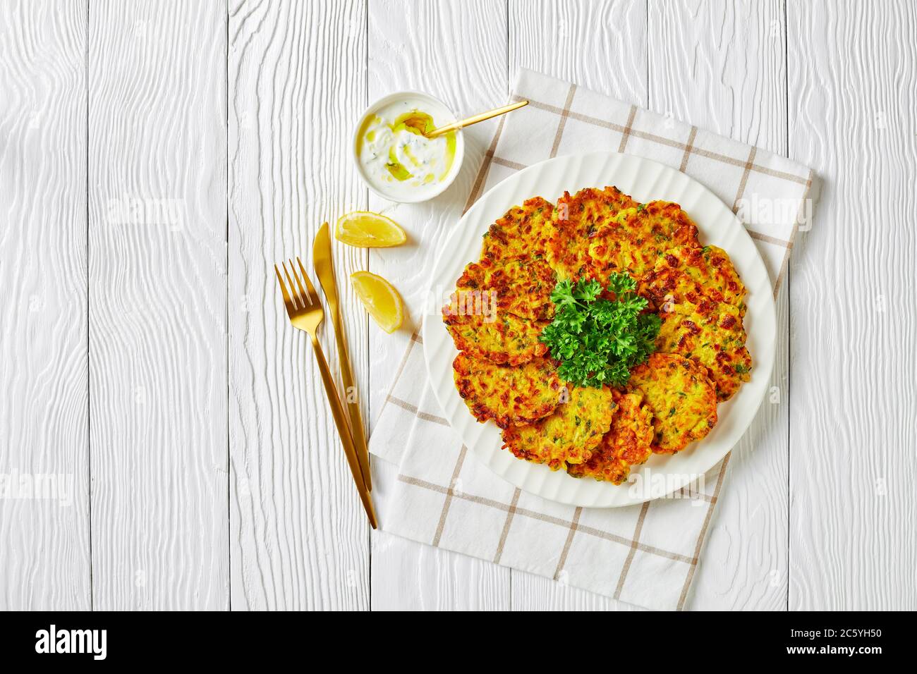 Keto Diätgericht: Süße Zwiebellatten oder Pfannkuchen mit Gemüse und Reis, serviert auf einem weißen Teller mit Petersilie und Joghurt-Sauce auf einem weißen Holzbackgroun Stockfoto