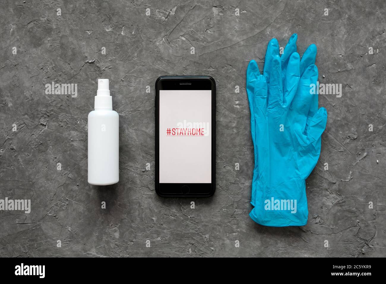 Das Konzept des Aufenthalts zu Hause ist die Epidemie des Coronavirus covid-19. Antiseptische und medizinische Handschuhe und Telefon auf grauem Hintergrund. Ansicht von oben Kopierbereich. Stockfoto