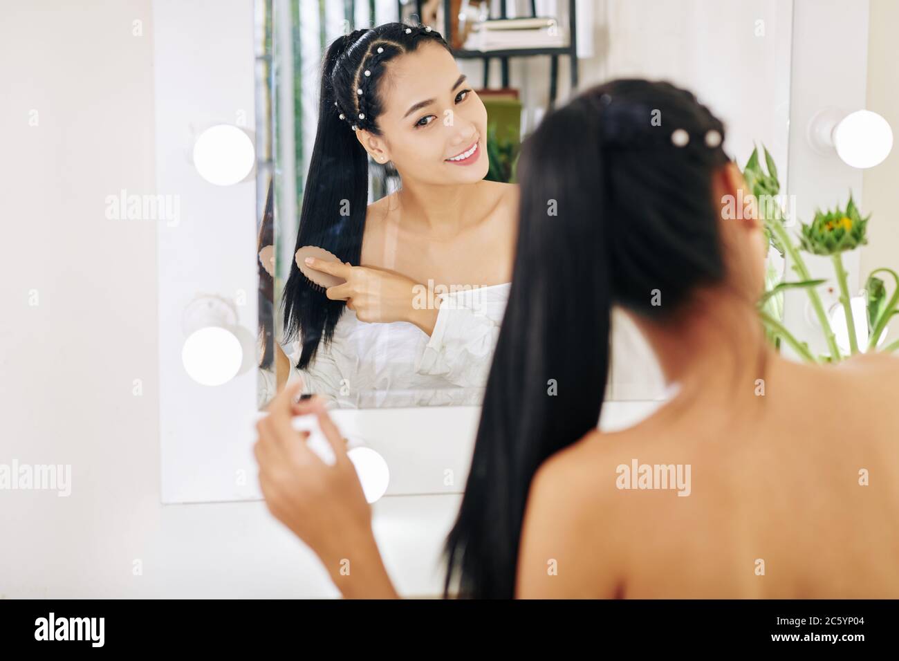 Lächelnd hübsche junge asiatische Frau, die Haare vor Eitelkeit putzt Stockfoto