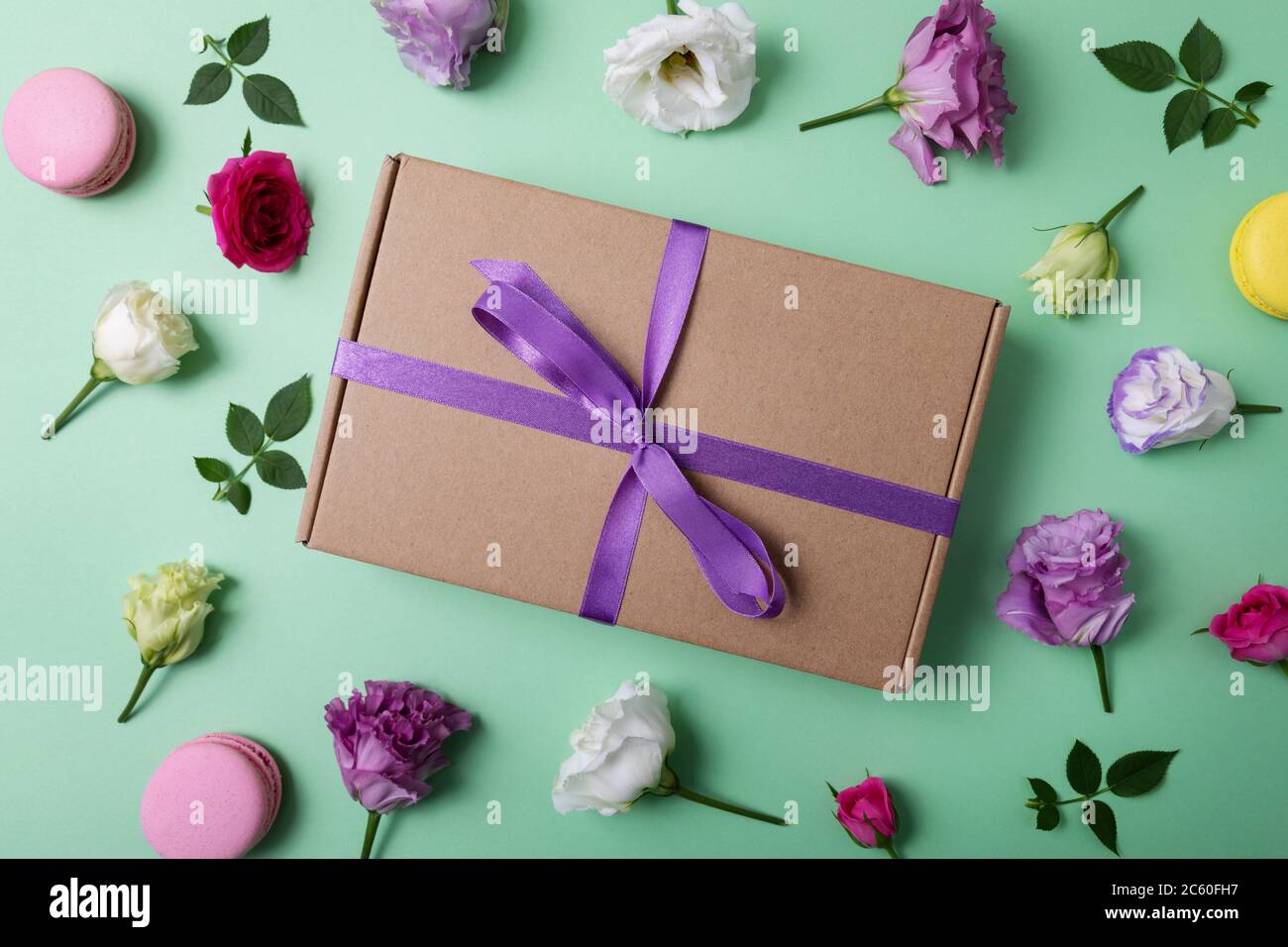 Geschenkbox mit lila Band und Blumen auf grünem Hintergrund. Draufsicht Stockfoto