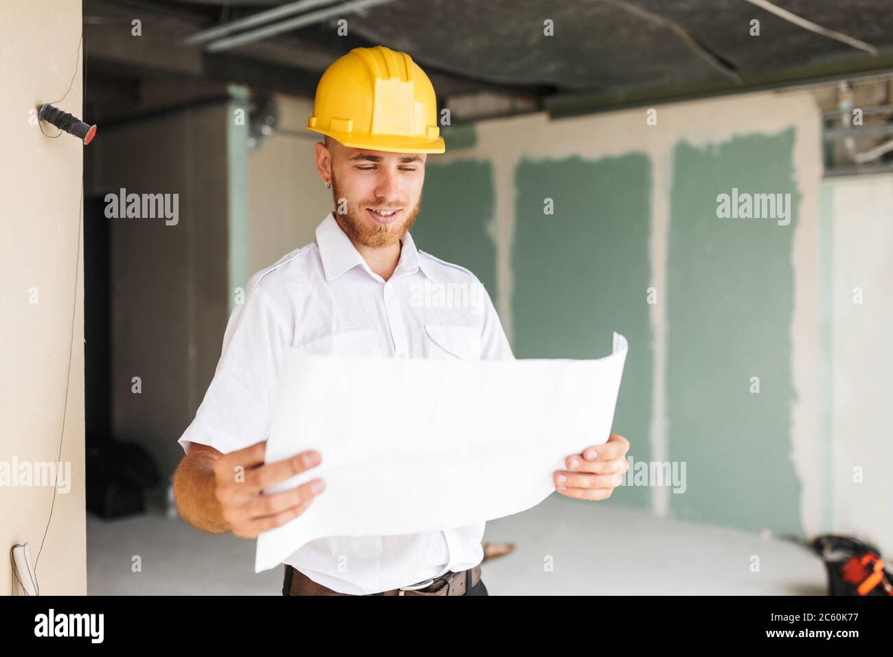 Junger Architekt in weißem Hemd und gelbem Hardhut glücklich lookin Stockfoto