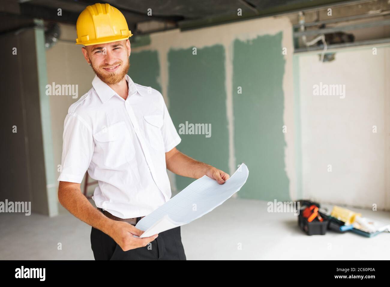 Lächelnder Architekt in weißem Hemd und Hardhut, der freudig auf sich schaut Stockfoto