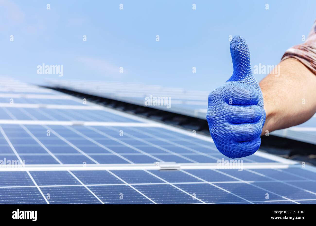 Männlicher Arbeiter zeigt Daumen nach oben, positive Geste gegen Solarpanel, Solarstation. Wie alternative Energie Sonnenenergie Energie. Mann installiert Solar Stockfoto
