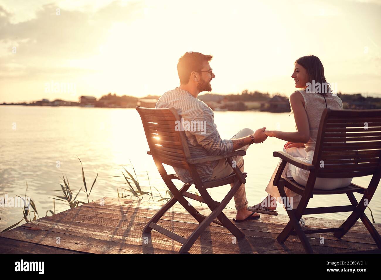 Romantisches kaukasisches Paar auf Stühlen am Fluss sitzend, Hände haltend, sprechend, einander beobachtend. Raum kopieren Stockfoto