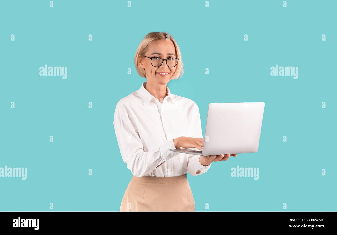 Selbstbewusste Geschäftsfrau mit einem lachenden Laptop vor blauem Hintergrund Stockfoto
