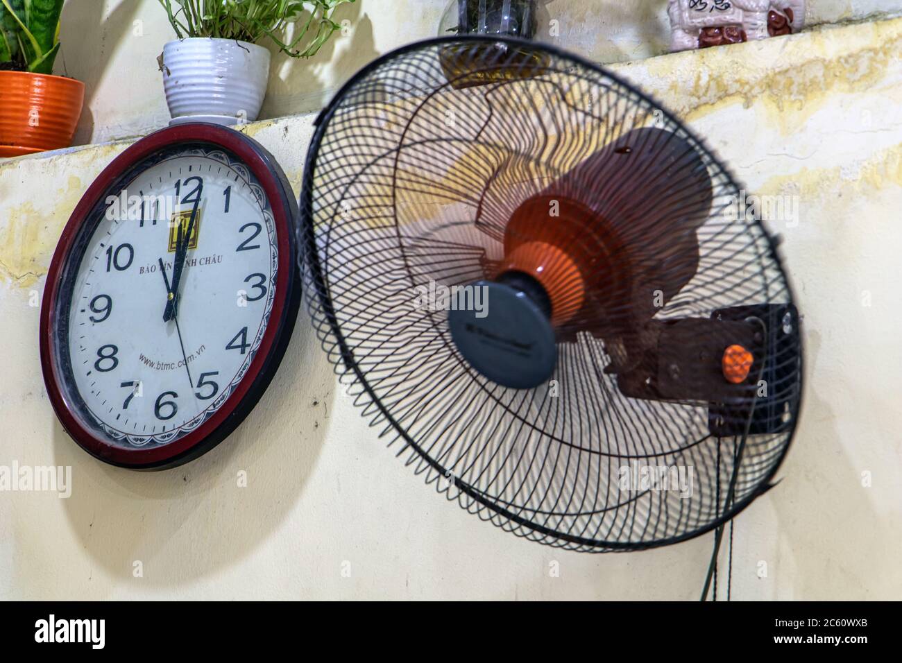 HANOI, VIETNAM, APR 20 2019, Uhr hängt an der Wand neben einem drehbaren Ventilator im Café Stockfoto