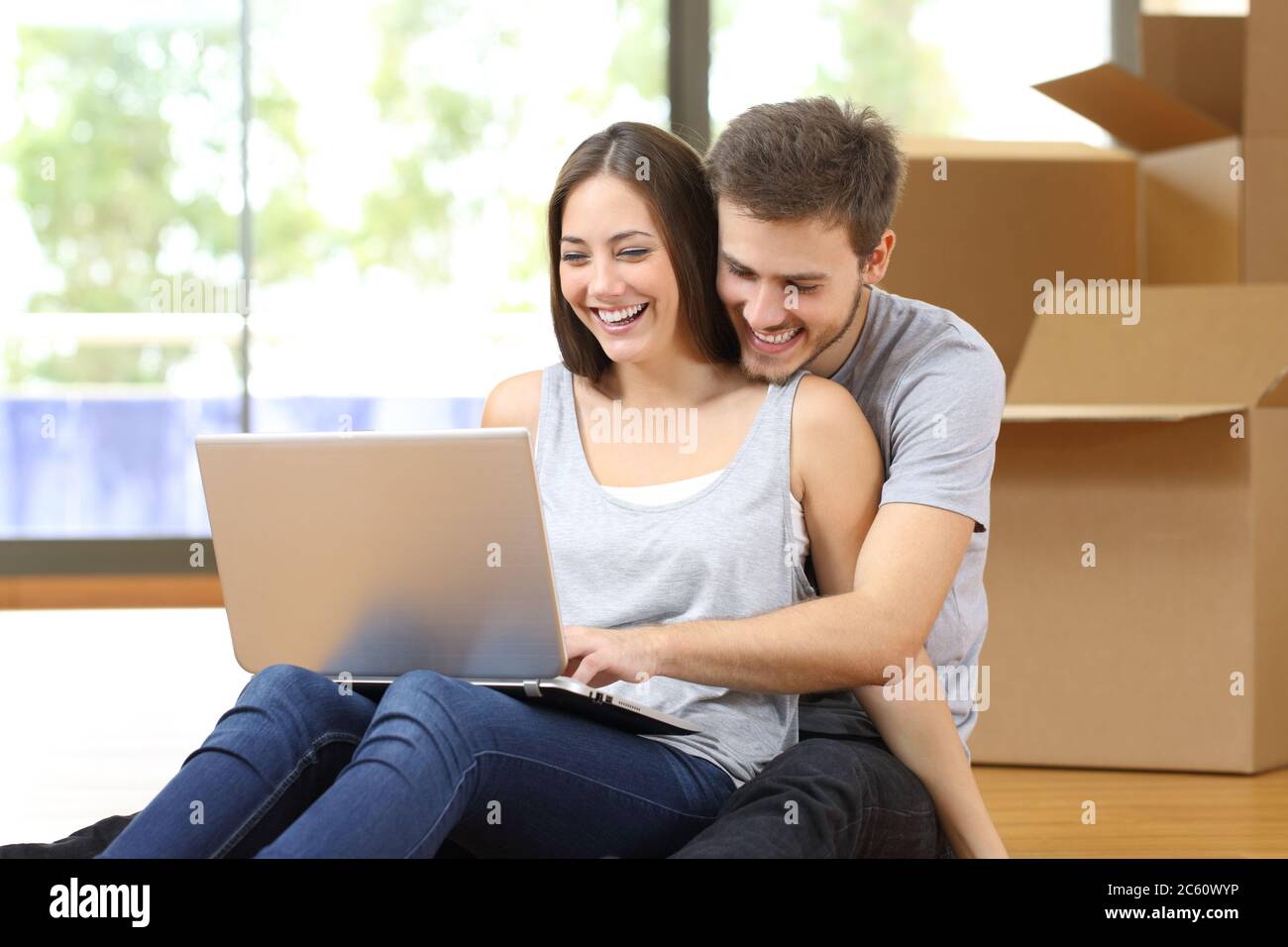Glückliches Paar mit Laptop Umzug in ein neues Zuhause umgeben von Boxen sitzen auf dem Boden Stockfoto