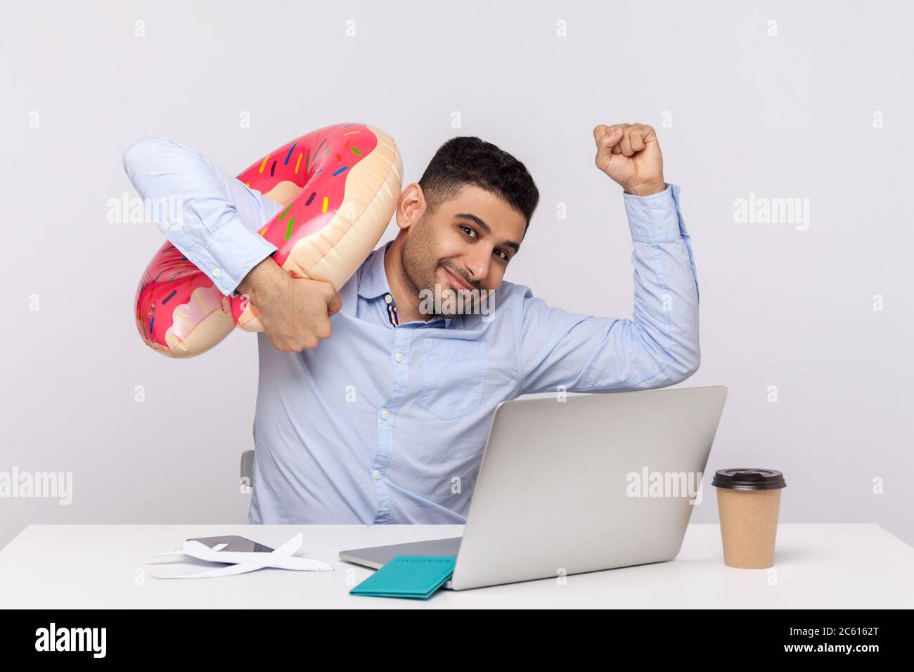 Ein glücklicher Mitarbeiter, der die Hände hebt, um mit Gummiring von seinem Büroarbeitsplatz wegzulaufen, sich beeilen, um sich auf Wochenendausflug, Reise und Urlaubsreise auszuruhen. Stockfoto