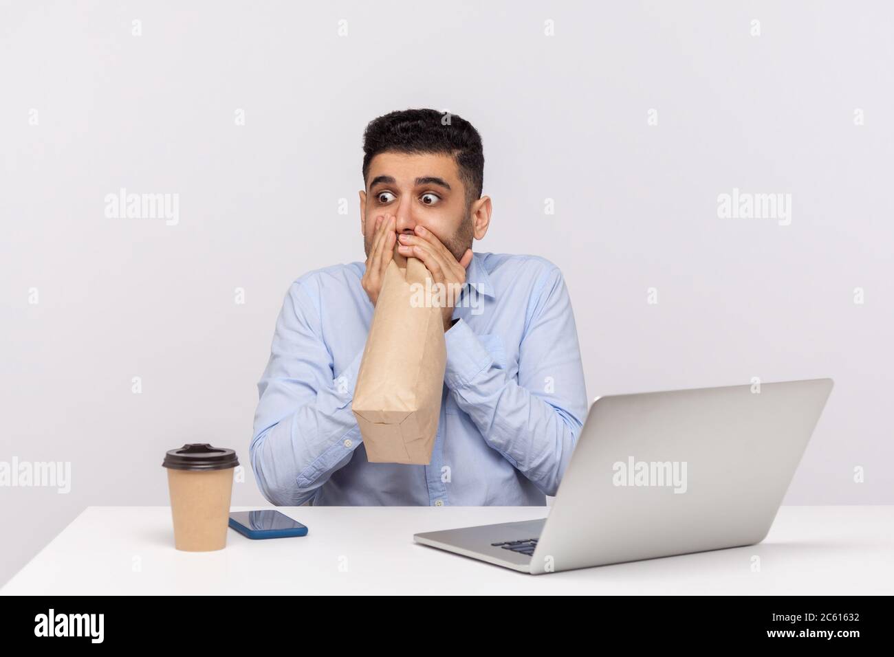 Erschrocken Mann Mitarbeiter sitzen im Büro Arbeitsplatz mit Laptop, Ausatmen und Einatmen in Paket, mit Papiertüte, um das Wohlbefinden zu verbessern, Überwindung str Stockfoto