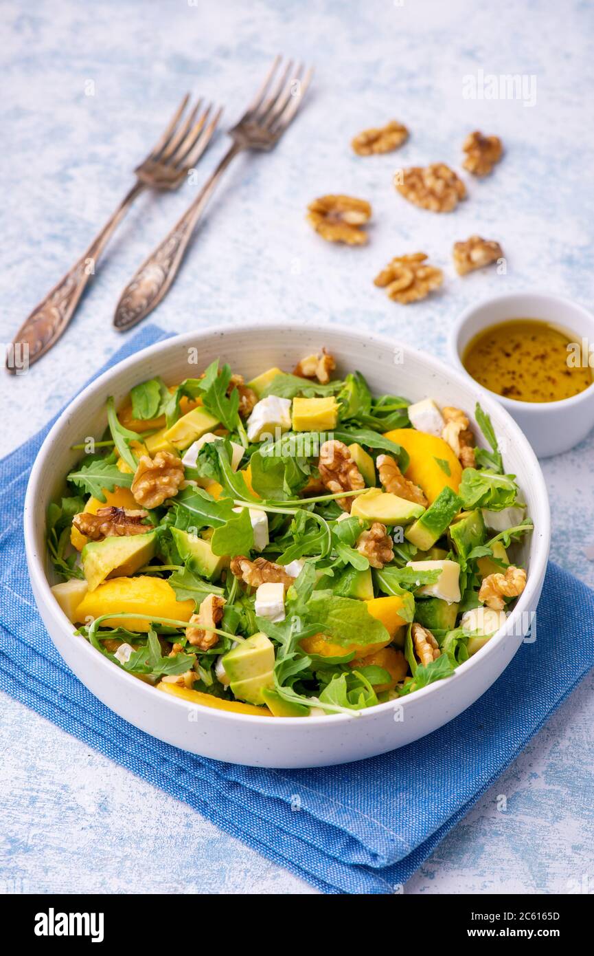 Rucola Salat mit Pfirsichen, Avocado, Camembert und Walnüssen, auf hellem Boden. Stockfoto